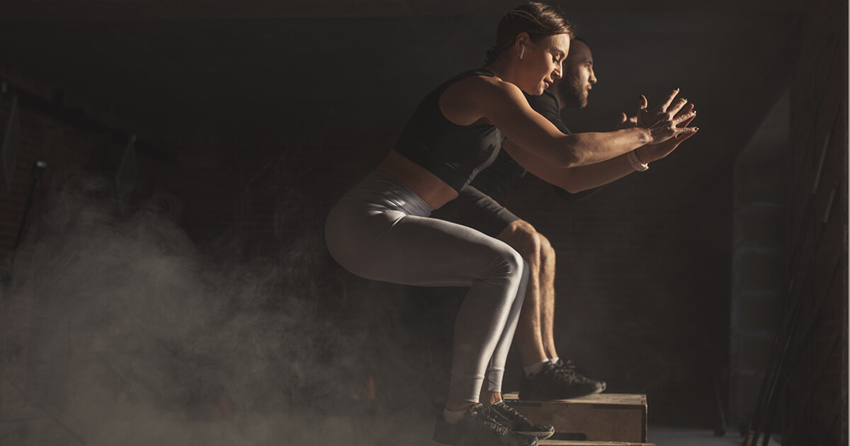 Dwie osoby wykonujące skoki na boksach podczas treningu crossfit w przyciemnionym pomieszczeniu nb-trening-crossfit-ckmpl-1200x630
